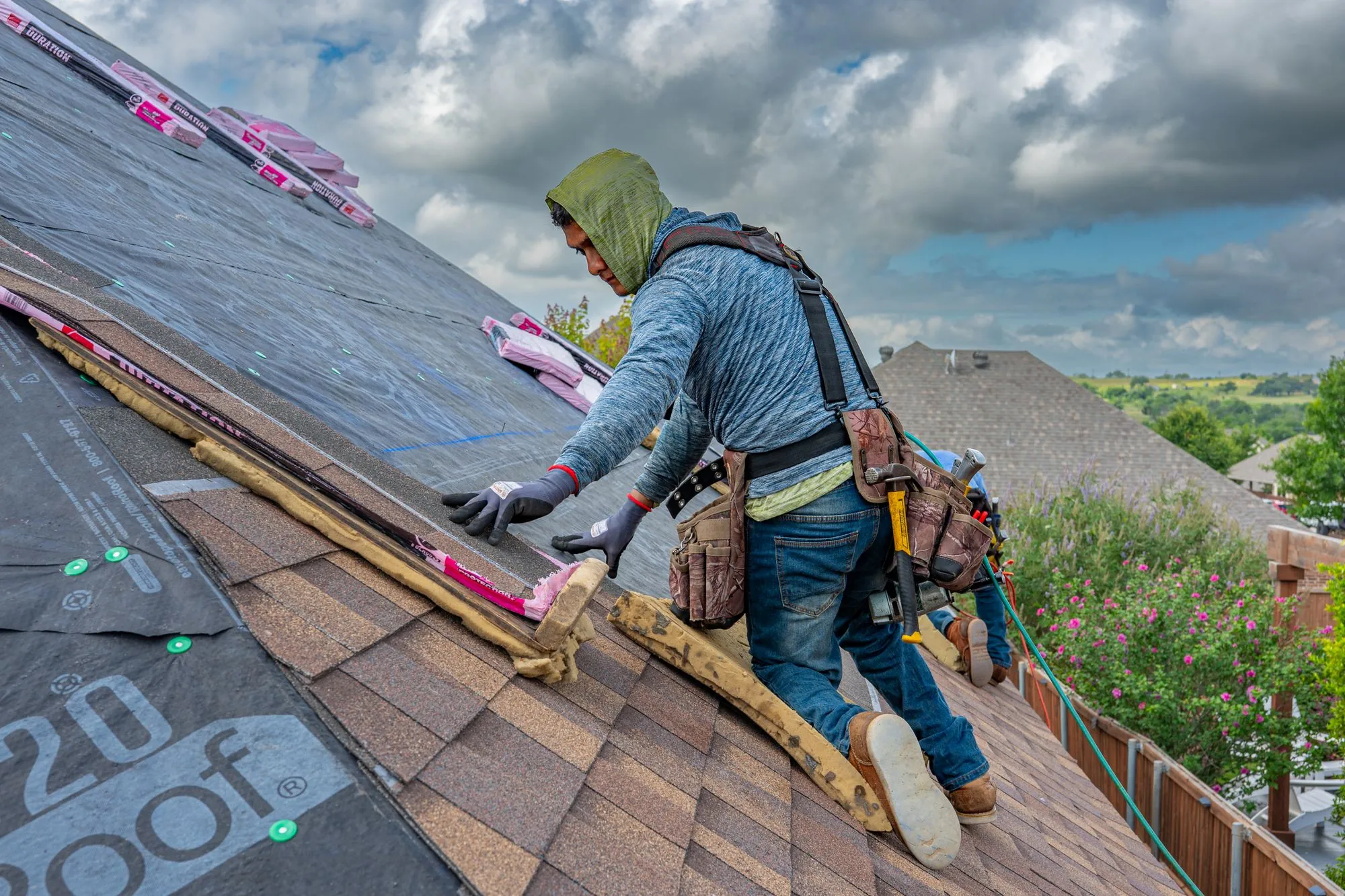 A roofer working a course of architectural shingles with a flat bar, tool belt on