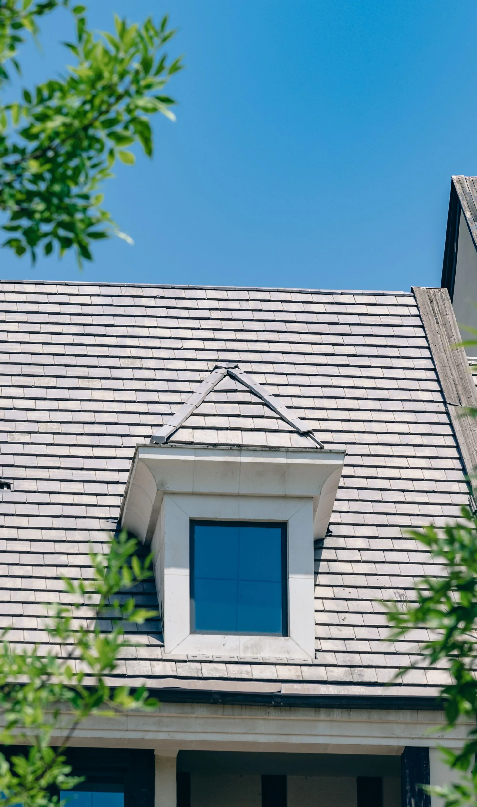 A shingled house with a dormer window against a clear blue sky