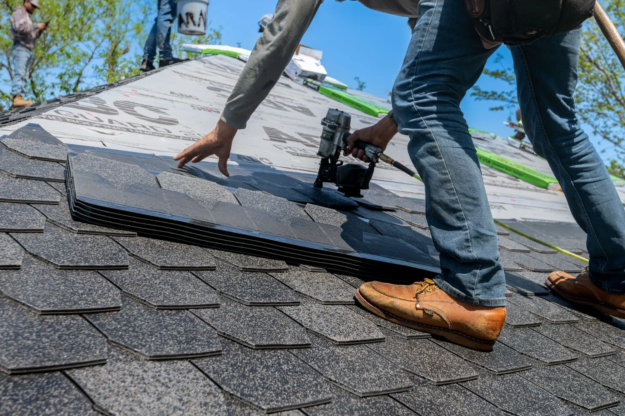 Hands setting a shingle and driving it home with a nail gun