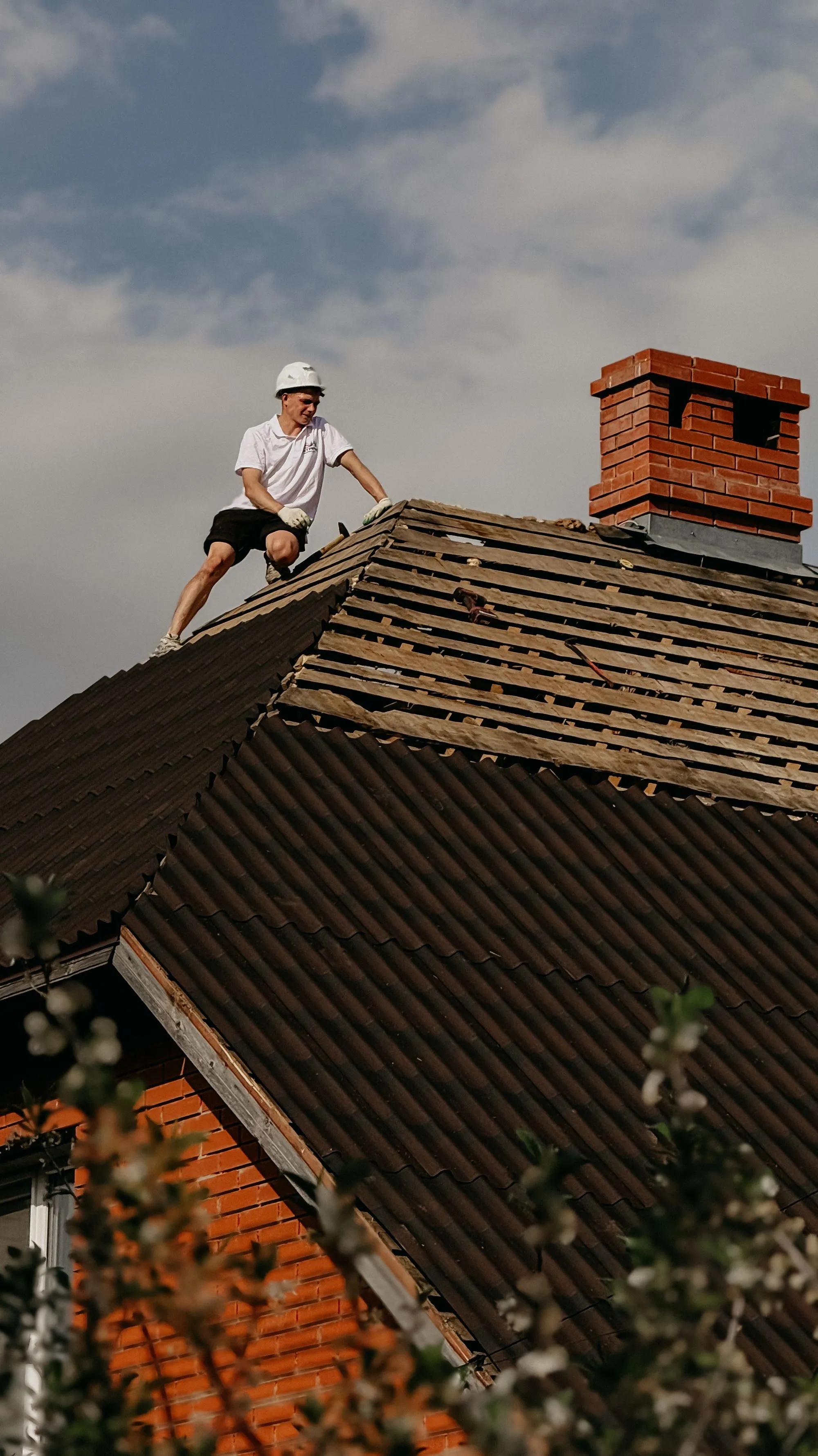 A roofer working along the ridge of a house beside its chimney