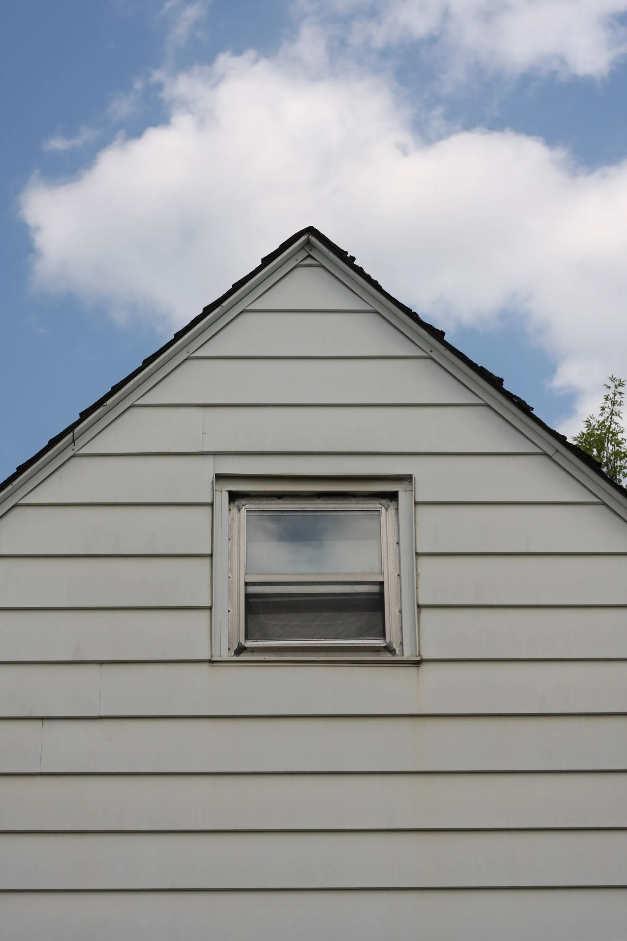The sided gable end of a house with a single window