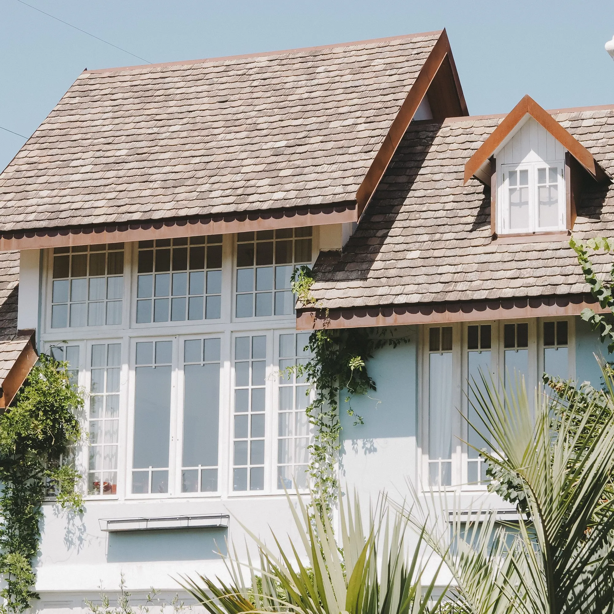 A sided house with dormers and a shingled roof in sunlight